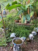 Wide view of garden showing bird bath, frog statues, bird statues, plants, and bird feeder pole.