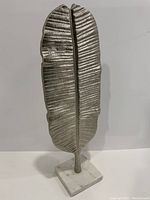 Metal leaf sculpture with detailed texture and silver finish, mounted on a rectangular white marble base