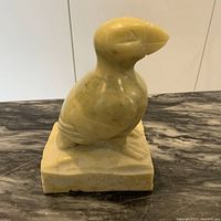 Angled front view of the stone bird sculpture on rectangular base showing detail of carving and color of the stone.