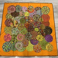 Full view of the large silk scarf laid flat, showing vibrant, multicolored spiral circle designs on an orange background.
