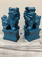 Two large ceramic foo dogs with turquoise shiny underglaze and felt-lined square bases next to water bottle for scale