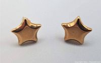 Front view of the pair of small star-shaped yellow gold earrings on a white background, showing their shape and polished finish.