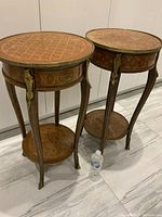 Pair of circular mahogany lamp tables shown side by side with ormolu mounts and lower shelves.