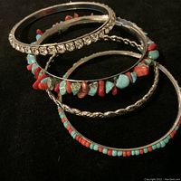 Set of four bangles including rhinestone, twisted metal, and turquoise/red bead designs on black background