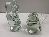 Two clear glass animal figurines, one abstract and one bird-shaped, displayed on white surface.