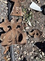Rust-colored cast iron architectural fragments on gravel ground, showing rust and weathering with mounting holes visible.