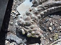 Close-up of cast iron architectural piece with round clustered detail, weathered surface with remnants of paint or finish, lying on the ground.