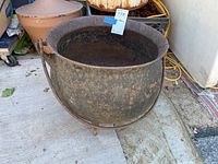 Front angle view of antique cast iron cauldron showing rounded body, rim, and handle with rust and wear