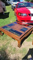 Square Asian style wooden coffee table placed outdoors on grass, showing glass inset panels and decorative floral inlay
