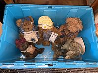 Top-down view of five collectible bears in a blue plastic bin showing various clothing and fur textures.