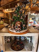 Overview of lighted Boyds Bears Christmas tree figurine on wooden shelf with some mugs and the plate below.
