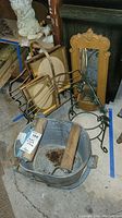 Wide view of vintage galvanized mop bucket with wooden handles, brass magazine rack, a large mirror with ornate gold frame, green framed mirror planter, wrought iron plate stand and picture frames stacked near them.
