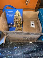 Box with approximately 50 copies of Christmas In Bethlehem books stacked inside, showing the front cover with a lit Christmas tree and scenic Bethlehem image.