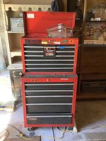 Front view of red metal tool chest with open top lid, multiple drawers, and stickers on front