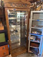 Full view of tall wooden curio cabinet with glass door and sides, showing decorative scrollwork on top and four glass shelves inside.