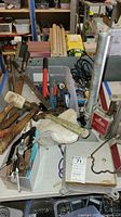 Various hand tools including files, hammers, mallet, hatchet, caulking tools, clamps and Dayton drill press stand parts on table.