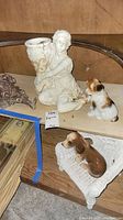 Top down view of porcelain woman figure holding vase, two dog figurines including one on a wicker chair