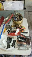 Overall lot view of assorted hand tools including a metal bucket filled with various metal tools, red-handled screwdrivers, clamps, staplers, and black plastic items.