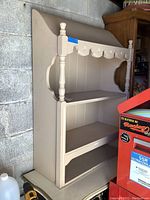 Full view of wooden 3-shelf hutch painted cream with scalloped top and decorative sides.