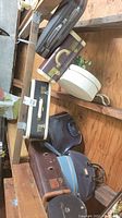 Photo of multiple vintage travel cases including hard luggage, wig cases, and antique doctors' travel bag on a wooden shelf.