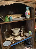 Shelf displaying multiple glass and ceramic items including milk glass bowl, plate, glass flower basket, vases, painted flower vase, and owl figurine pin cushion