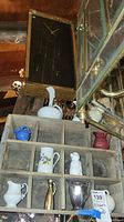 Full view of seven miniature pitchers displayed in a wooden divided crate with sections, showing size and materials of each pitcher