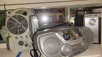 Philips AZ1301 CD boombox, Panasonic radio cassette player, radio/fan/light device, and box of electronic tubes together on shelf