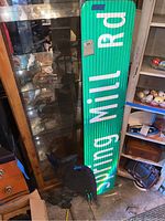 Photo showing the green Spring Mill Rd street sign leaning against a glass cabinet and surrounded by other items.