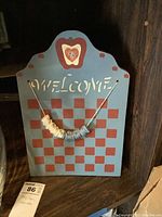 Hand-painted wooden welcome sign with apple motif and checkerboard background, with string of circular beads