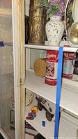 Shelf with decorative tins, toy wagon, wind-up bird toy, and miscellaneous items inside glass cabinet