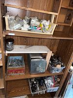 Wooden shelving unit with various bins containing small metal hardware parts and a vintage chrome paper towel dispenser on a middle shelf.