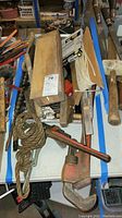 Various wrenches, coiled rope, wooden handled pipe wrench, and metal hand tools piled together