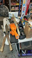 Photo showing variety of yard and power tools including Black & Decker hedge trimmer, garden shears, battery charger, and miscellaneous items on table.