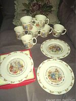 Full set of 7 plates (one boxed) and 7 mugs arranged showing Bunnykins Celebrate Your Christening designs