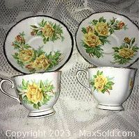 Front view of two teacups and two matching saucers with yellow tea rose design and gold trim on white porcelain.