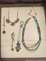 Five vintage necklaces arranged against a white background showing various styles, colors, and materials including turquoise beads, coral beads, silver and gold tone metals.