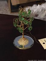 Full view of the green crystal gem tree on a round faceted glass base, showing gem details and wire branches.