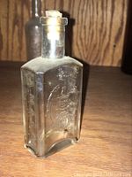 Front view of clear glass medicine bottle embossed with ornate design.
