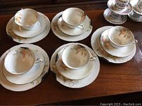 Five sets of hand-painted antique china teacups, saucers, and plates arranged on a wooden surface showing the floral pattern and gold trim.