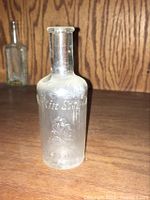 Clear glass bottle with embossed 'Larkin Soap Co' lettering and emblem sitting on a wooden surface with a darker bottle in the background.