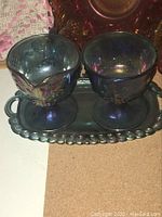 Blue carnival glass creamer and sugar bowl on tray showing Harvest Grape pattern and iridescent finish.
