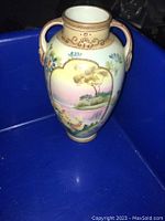 Front view of oval-shaped Nippon vase with scenic landscape hand painted design and dual handles.