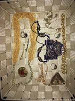 Overview photo showing varied vintage/retro fashion jewelry including necklaces, rings, brooches, and bracelets laid in woven basket.