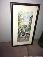 Photo of framed Lucien Delarue print showing Paris street scene with Arc de Triomphe and cafe with umbrellas