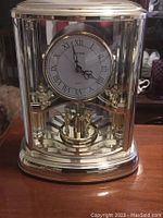 Front view of Rhythm mantel clock with clear casing and gold-tone features, clock face with Roman numerals.