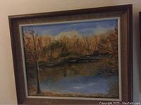 Framed oil painting showing autumn landscape with lake and trees, overall frontal view.