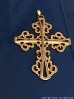 Close-up image of the vintage gold-tone cross pendant showing intricate scrollwork and hollow cutouts on each arm, on a dark blue background.