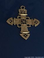 Single vintage cross pendant with metal intricate pattern, photographed on a dark blue surface.