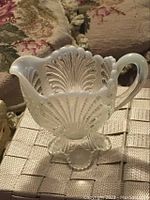 Side view of frosted glass creamer showing shell pattern and handle