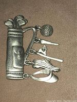 Front view showing golf bag brooch detail and dangling charms including ball, tee, flag, shoe, and club